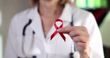Doctor holding in his hands red ribbon symbol of fight against HIV and AIDS closeup 4k movie slow motion. Stop hiv aids concept