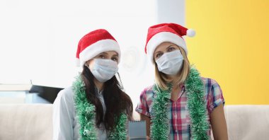 Koruyucu maskeli iki kadın yan yana oturup 2021 takvimini bekletiyor. Satılık Noel ve yeni yıl süslemeleri.