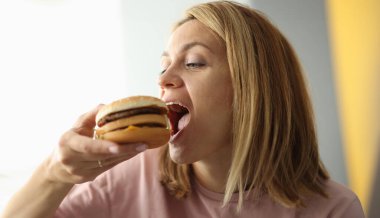 Genç bir kadın ağzını açık hamburgerle ısırdı. Sağlıksız yiyecek fast food konsepti.