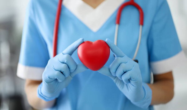 Doctor in blue suit, gloves and with red stethoscope hold symbol. Shape red heart close up.