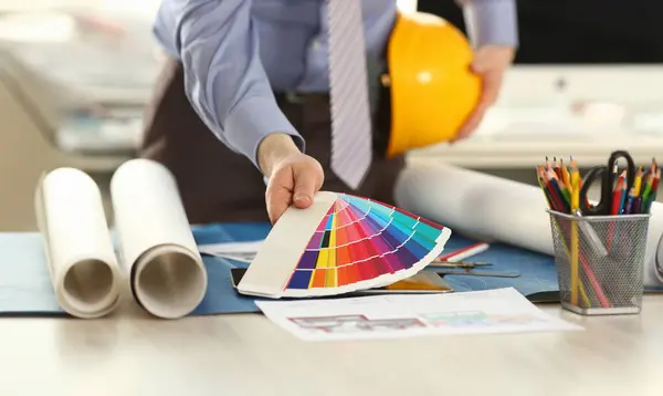 Architect Holding Spectrum Color Palette at Office. Male Employee Engineer, Building Decorator with Yellow Hard Hat in Hand. Drafting with Architectural Instruments and Accessories