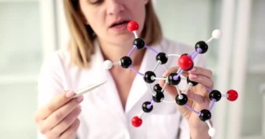 Bir biyokimyacı kadın bir moleküler model gösteriyor, yakın plan. Eğitim, moleküler formül tanımı