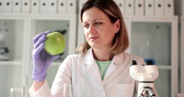 Bir kimyager kadın yeşil bir elmaya yakından bakar. Laboratuvarda yeni bir ürün oluşturulması, seçim