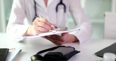 Masada oturan doktor dosyanın üzerine yakın plan bir yazı yazıyor. Terapiste git, yüksek baskı yap.