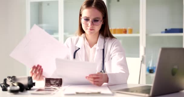 テーブルで医者をしている若い女性が書類 クローズアップを見ている 健康診断の結果 — ストック動画