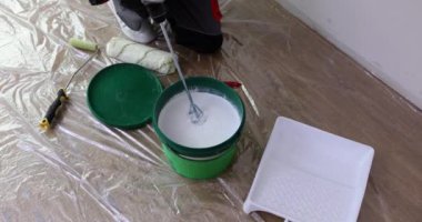 Odadaki usta bir kovada boya karıştırıyor, apartman yenileniyor. Evin duvarını boyamak.