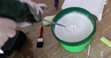Odadaki müteahhit boyayı çırpıcıyla karıştırıp tamir ediyor. Duvara beyaz boya