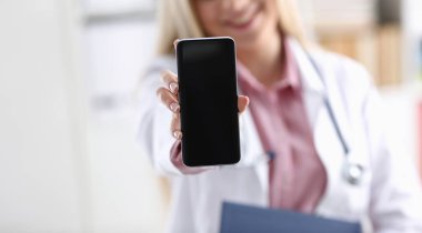 Güzel kadın sarışın doktor Smartphone elinde hastalığı tartışmak ve bir uzaktan eğitim mobil reklam uygulaması için bir online konsültasyon veren kadın ofis tutmak.