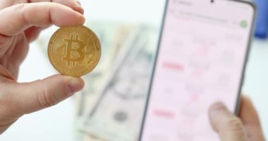 Elinde altın Bitcoin tutan ve cep telefonunun yakın plan 4K filminde büyüme grafiklerini izleyen bir adam. Kripto döviz kuru kar oranı kavramı