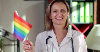 Gülümseyen kadın doktor klinik 4K filminde ağır çekimde Igbt bayrağı sallıyor. lgbt topluluk konsepti için tıpta güçlendirme