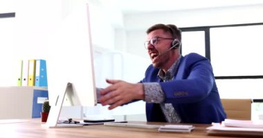 Kulaklıklı bir iş adamı bilgisayar ekranına bağırıyor ve orta parmak 4K filmi gösteriyor. Uzak çalışma kavramının sorunları ve güçlükleri