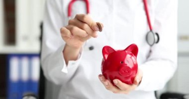 Doktor domuz kumbarasına kırmızı domuzla para atıyor. Yaşam ve sağlık sigortası kavramı