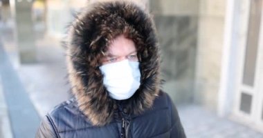 Sıcak kışlık ceketli ve koruyucu maskeli bir adam caddede yürüyor. Sağlık koruma ve maske modu kavramı