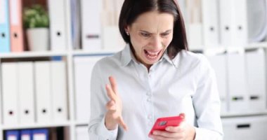 Kızgın kadın telefon ekranına bakıyor ve ofis 4K filminde yavaş çekimde bağırıyor. Taşınabilir internet sorunları kavramı
