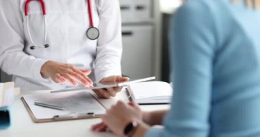 Doktor, hastanın önünde dijital tabletle ilgili bilgileri inceliyor. 4K yavaş çekim. Tıp konseptinde modern teknolojiler