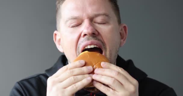 おいしい食欲をそそるハンバーガーを食べ 4K映画スローモーションを楽しんでいる若い男 不健康な食の概念 — ストック動画