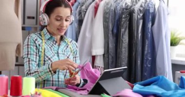Kulaklıklı kadın tasarımcı atölyedeki işyerinde kumaş kesiyor. Kıyafet konsepti koleksiyonu oluşturuluyor