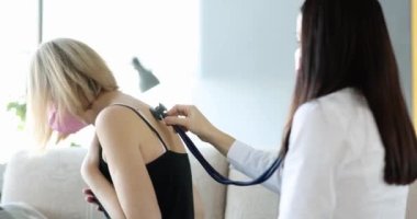 Doktor evde maskeli güçlü öksüren kadının ciğerlerini steteskopla dinliyor. Zatürree ve bronşit kavramı