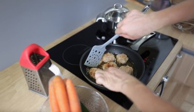 Fried cutlet in the hands of a cook against the background of a frying pan and an electric stove. Cooking meat products at home