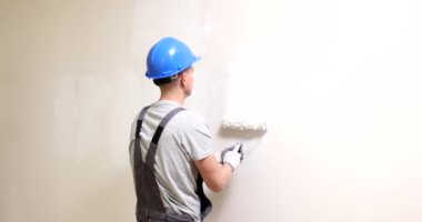 Duvarı silindirle boyamış bir adam. Beyaz boyalı bir daire ya da ofis tadilatı.