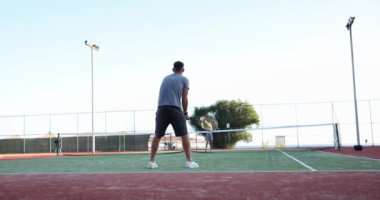 Açık hava tenis kortunda iki profesyonel tenisçi. Sporcular tenis oynarken çok sıkı çalışırlar. Raketle topa vurup yakalamaya konsantre olurlar.