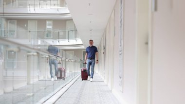Bavullu genç adam otel koridorunda yürüyor. Yurtdışında turizm ve eğlence kavramı