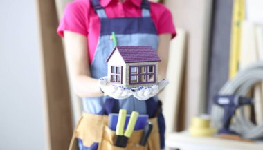 Oyuncak ahşap evi elinde tutan kadın müteahhit. Ev inşaatı ve onarımı