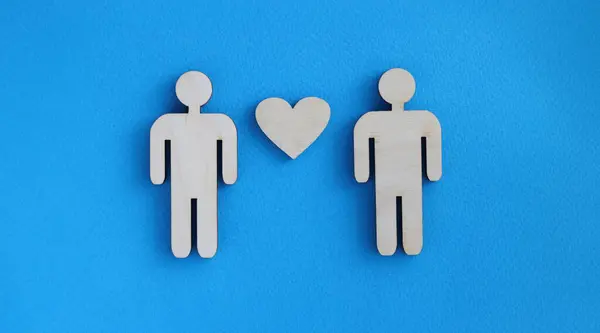 Wooden toy men and heart lying on blue background. Love between men concept