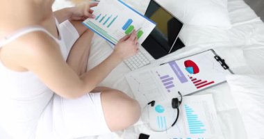 Yatakta yatan bir kadın istatistiksel bir rapor tutuyor, yakın plan. Ofis çalışanı yatak odasında çalışıyor.