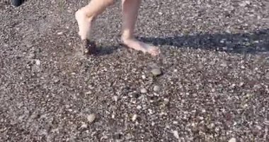 Bir kadın denize gider, bacakları yakın, yavaş çekimde. Temiz su, çakıl taşı plajı, turizm, doğal ışık.