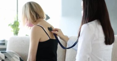 Doktor öksüren bir kadının akciğerlerini dinliyor, yakın plan. Koronavirüs ve zatürree belirtileri.