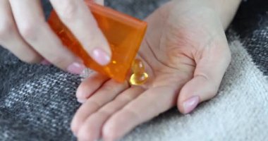 Bir kadın kavanozdan sarı kapsüller dolduruyor, elleri yakın çekim. Gıda takviyeleri, omega 3, sağlık desteği
