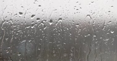 Yağmur damlaları cama vurur, yakın plan. Yoğunluk gri arka planda akar, mevsimsel yağış