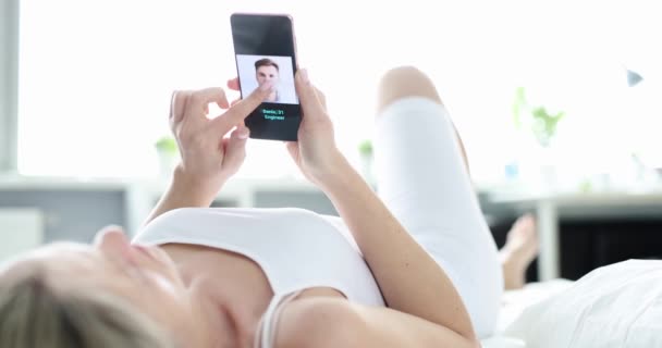 床上的女人用智能手机在网上的应用程序中选择一个男人 因特网日期 婚介机构 — 图库视频影像