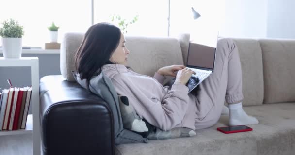 一个女人躺在家里的沙发上 带着笔记本电脑 动作缓慢 休息学习 放松周末 远程工作 — 图库视频影像