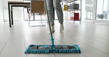 Ofiste bir kadın yerleri paspasla yıkıyor, bacakları yakın plan. Çalışma alanının dezenfeksiyonu, temizlik