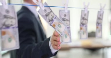 Bir iş adamı mandalda asılı duran dolarlara dokunur, yakın plan. Suç faaliyetlerinin geliri