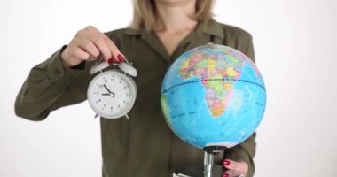Bir kadın elinde bir küre ve çalar saat tutuyor, yakın plan. Kavram, dünya zamanı, Greenwich meridyeni