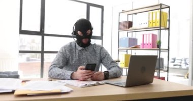Ofiste, maskeli bir dolandırıcı telefonla konuşuyor, yakın plan. Telefonla dolandırıcılık devresi, ön görünüm