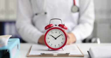4K numaralı klinikteki doktor masasında duran kırmızı alarm saati ağır çekimde. Klinik çalışma saatleri kavramı