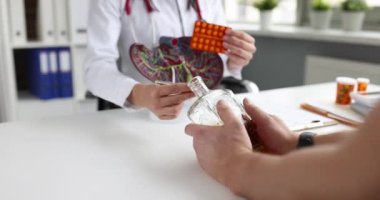 Doktor, hastaya karaciğer ve hapların yapay modelini gösteriyor. Bir şişe alkollü 4K film ağır çekimde. Karaciğer sirozu teşhisi ve tedavisi