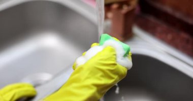 Eldivenli, sabunlu, köpüklü, yakın çekim 4K filmli sünger sıkan ev hanımı elleri. Temizlik servisi bulaşık yıkama konsepti