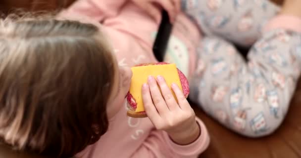 小女孩躺在沙发上 一边吃三明治 一边吃奶酪和香肠 慢动作 儿童适当营养概念 — 图库视频影像