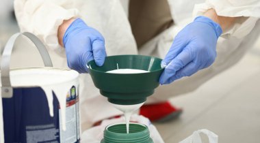 Yeşil plastik sulama tenekesini beyaz boyayla tutan kalifiye işçilerin yakın çekimi. Mavi koruyucu eldivenler. Dairenin yenilenmesi ve iç tasarımın değiştirilmesi. İnşaat alanı kavramı