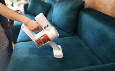 Kadınların el temizleme sehpası, küçük beyaz elektrikli elektrikli süpürge ile yeşil kanepe. Şık, deniz mavisi bir kanepe. Yenileme ve iç tasarım. Ev hanımı ya da temizlik hizmeti konsepti