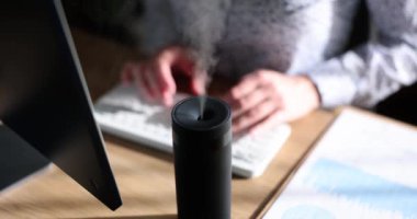Serbest çalışan bir kadın, ofisteki işyerinde dizüstü bilgisayarla nemlendirici kullanıyor. İş yerinde ya da evde iklim kontrolü