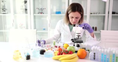 Mikroskoplu ve test tüplü kadın bilim adamı laboratuvarda bir sürü meyve ve sebze üzerinde çalışıyor. Laboratuvarda uyuşturucu ve ekipmanlı organik gıda