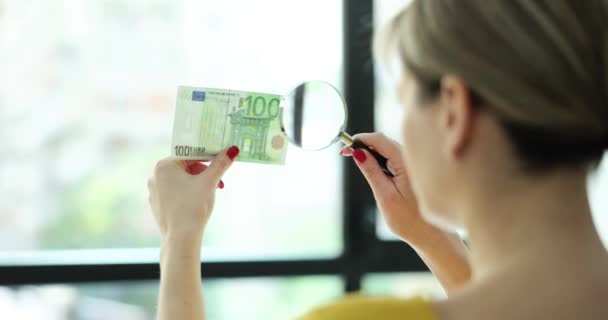 女人透过放大镜看100欧元钞票 女孩检查钞票的真伪 — 图库视频影像