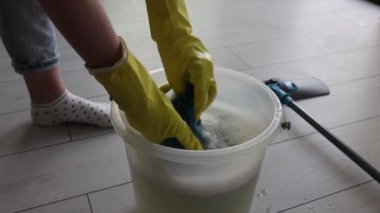 Elin ıslak bezi bir kova sudan çıkarıyor. Ev hanımı ıslak bez çıkarıyor.