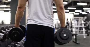 Spor salonunun arka gözünde dambılı olan erkek sporcu. Spor salonunda spor eğitimi.